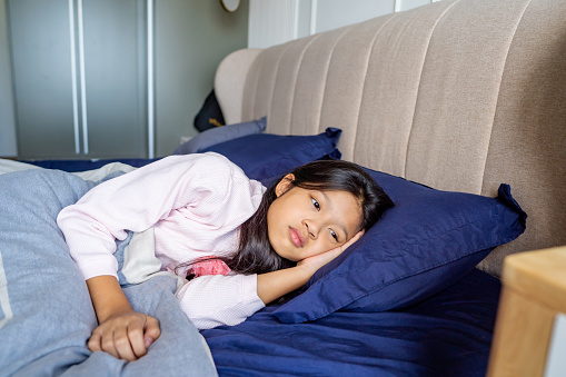 A little Asian girl is sick with a fever and covered with blanket having fever lying in her bed.