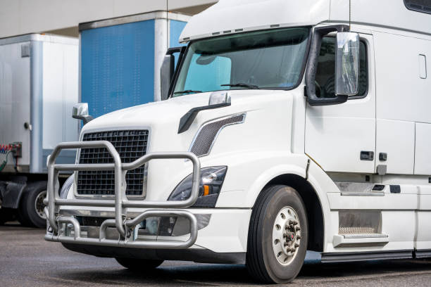 istock Bonnet white big rig semi truck with grille guard loading cargo standing in warehouse dock beside with another trucks and trailers 1475444087