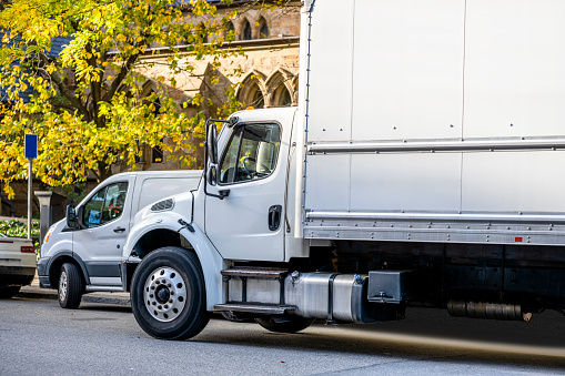 Industrial middle rig day cab semi truck tractor with box trailer and cargo mini van make  deliveries to customers standing on the city street according to the delivery schedule