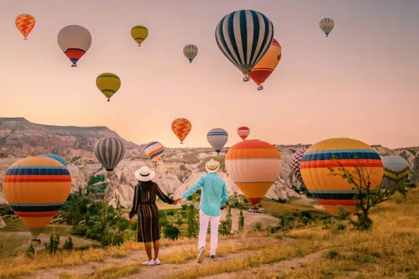 Photo of Cappadocia Turkey during sunrise, couple mid age men and woman on vacation in the hills of Goreme Capadocia Turkey, men and woman looking sunrsise with hot air balloons in Cappadocia