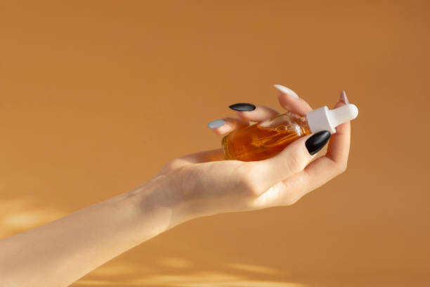 istock Woman's hand holds glass bottle with dropper cap on brown background. Bottle without labeling with orange serum for the face, cosmetic product. Concept of skin care and beauty 1475445209