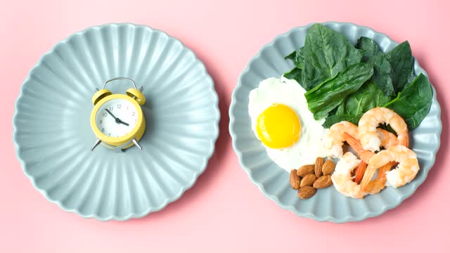 Plates with food and alarm clock on pink background top view, keto diet concept.