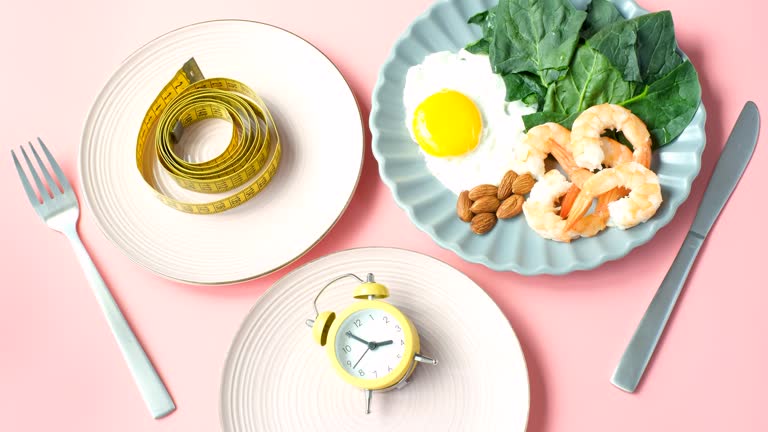 Three plates with food, alarm clock and centimeter tape and female hands on pink background intermittent fasting concept.