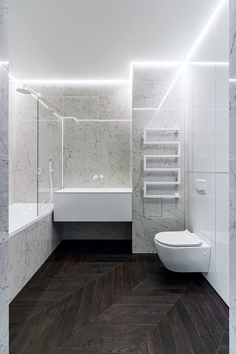 A luxurious interior in the bathroom with a bathroom, a shower on a shelf and a walk in the shower. White marble and dark brown floor. White cranes and plumbing.