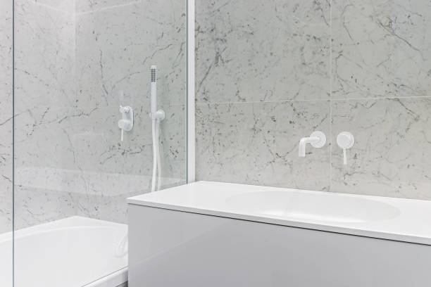 istock Modern bathroom with white faucets and shower, walls lined with white marble 1475449190