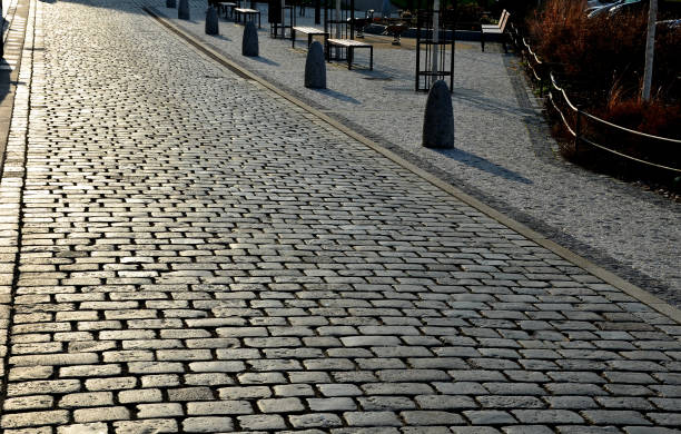 stone barriers in a square shaped cylinder with a hemisphere on top. granite curbs as stops at the parking lot. chain decorative fence against a colony of pedestrians and vehicles with a stone bollard