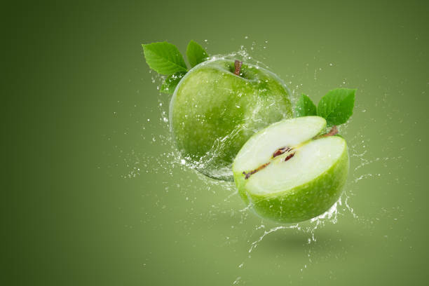 istock Creative layout made form whole and slice green apple and water splashing on a green background. 1475451610