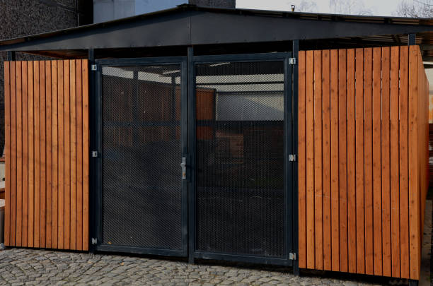 garage mit holzverkleidung und transparenter gittertür. müllabstellplatz in der nähe der pension. schützt das eigentum und die ordnung der bürger in der geschlossenen schutzeinrichtung. pkw-stellplatz sicher und ohne schnee, kopfsteinpflaster - wood bin stock-fotos und bilder