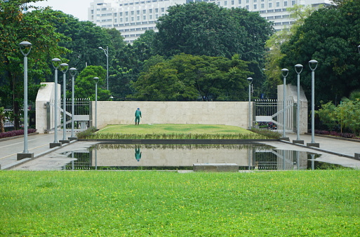 The view of the attendant watering the garden yard. This park is surrounded by greenery and several pillars of daytime garden lights in indonesia