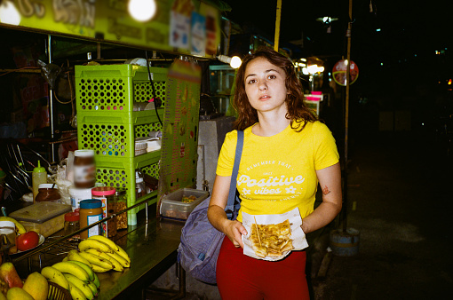 Young woman in yellow tank standing on night market. Shot with flashlight