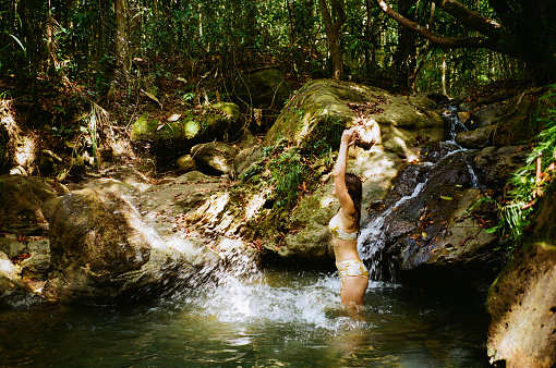 Cheerful woman swimming in waterfall in the jungles