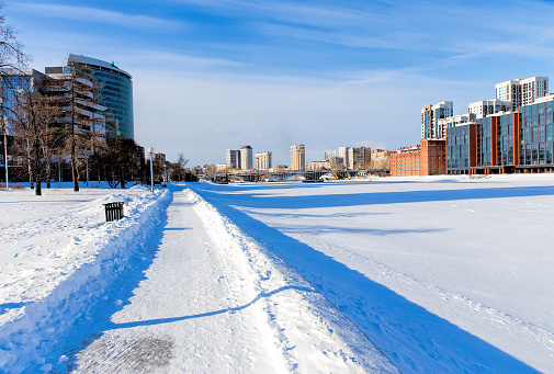 Snow-covered embankment on banks of a frozen river in center of a modern city