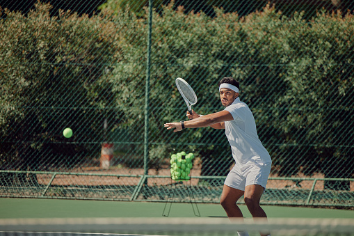 Indian man, sports or playing on tennis court in exercise, training or workout for competition, challenge or cardio games. Athlete, fitness or person hitting ball with racket in healthcare wellness