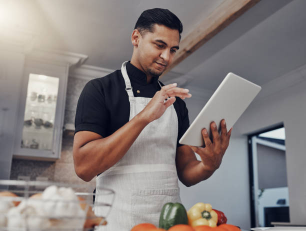 istock Man, cooking vegetables and tablet in kitchen while online with house wifi connection for learning or blog. Chef person with mobile app for online recipe for home food for vegan or healthy eating 1475461199