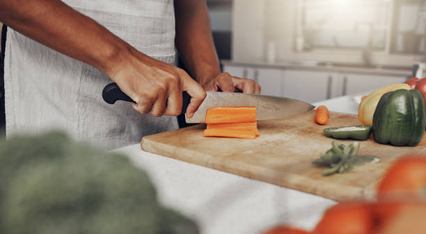 istock Hands, food and nutrition with a man cooking in the kitchen while cutting vegetables on a wooden chopping board. Salad, health or diet with a chef preparing a meal while standing alone in his home 1475462633