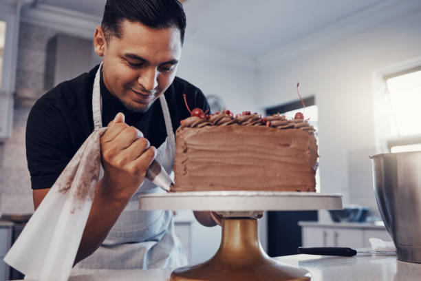 istock Piping, bakery and chef baking a cake with chocolate and pastry in a kitchen and is happy decorating his recipe. Food, dessert and cook preparing a sweet meal by a Brazil man and adds cream 1475462647