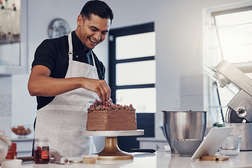 Chef, baking and cake with chocolate in a kitchen by a happy man preparing a sweet desert or a birthday. Decoration, baker or cook with a small business smiling and cooking dessert at a bakery