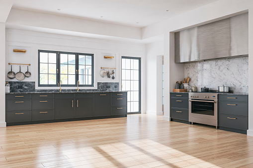 A side view of a retro anthracite, stainless steel, and marble kitchen on the hardwood parquet floor. Two golden elegant design wall lights, hung kitchen utensils and pans, and two golden faucets, in front of an old-fashioned french window and glass door on a side with a nice view of a luxurious garden and patio in the background.  A large stainless steel kitchen hood over a large stove with cooking pots and utensils. A white plaster ceiling with built-in reflectors. 3D rendered image.