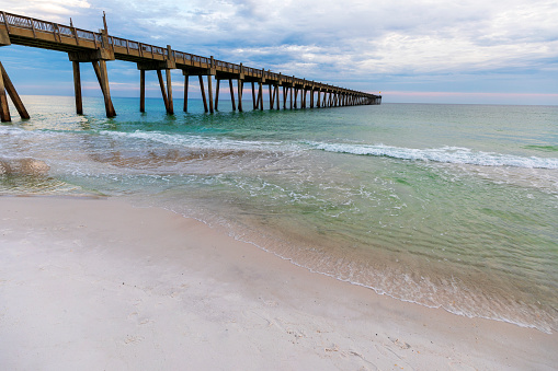 Pensacola Beach Fishing Pier extending out into the Gulf of Mexico during a pastel colored sunset sunset on a cloudy evening.