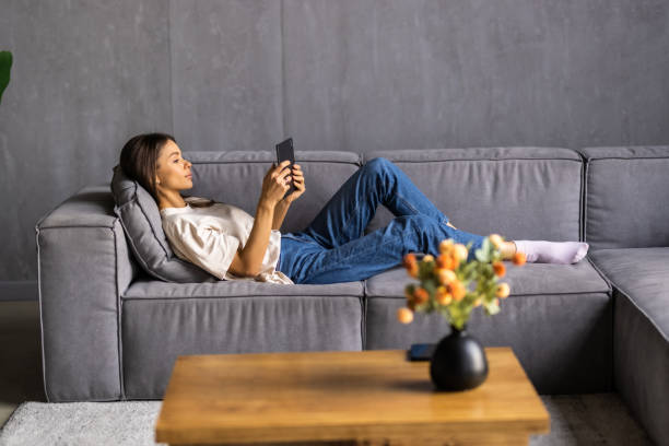istock Beautiful woman using a digital tablet and smiling while sitting on the couch at home 1475467265