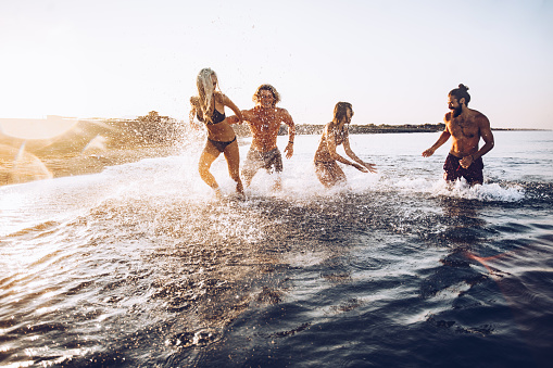 Group of happy people having fun while playing in the sea at sunrise.