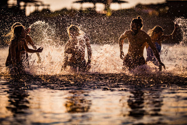 Young playful friends having fun while running and splashing in the sea at sunset.