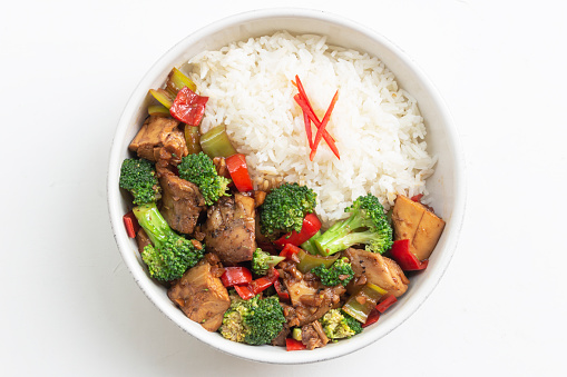 Stir fried chicken and broccoli bell pepper has rice in bowl on white wood table, top view, healthy food concept.
