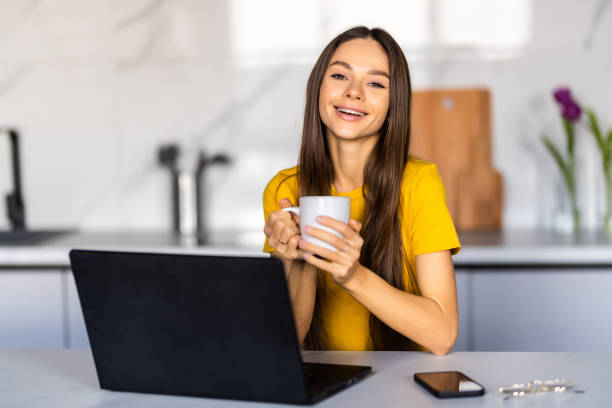 istock Beautiful woman in her kitchen during her breakfast. She is using her laptop. 1475475381