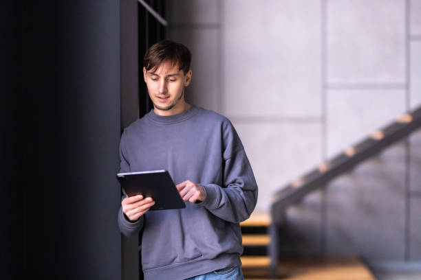 istock Young relaxed man sitting on coach in modern living room holding tablet computer checking social media, surfing internet, ordering food delivery, reading ebook at weekend. 1475477008