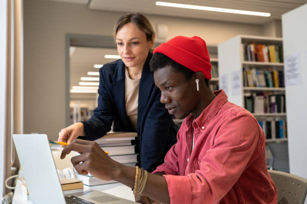 osobista nauczycielka pomagająca zdziwionemu, skupionemu czarnemu studentowi w rozwiązywaniu zadań na laptopie w bibliotece. - teacher preparation two people teamwork zdjęcia i obrazy z banku zdjęć