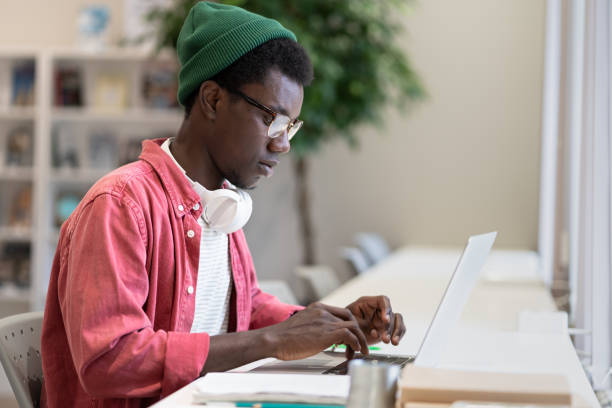 istock Young African American man freelancer working on laptop using public library as workspace 1475484537