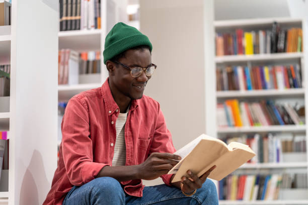 istock Interested African American student guy reading book in university library, studying for exam. 1475484548
