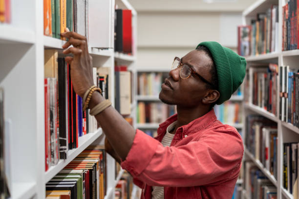 istock Puzzled concentrated black man student choosing need literature for study on bookshelves in library 1475484555