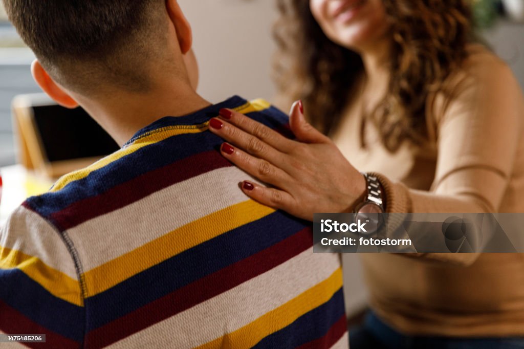 Mother holding hand on her son's shoulder while studying Close up shot of caring mother holding hand on her son's shoulder while assisting him homework and studying together. Teenager Stock Photo