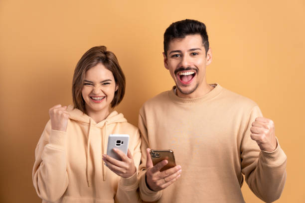 istock fun couple watching video and photos on mobile smartphone in beige studio background. network, messaging, internet concept. 1475488200