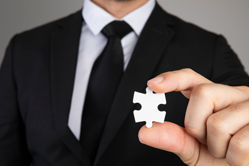 Businessman is holding puzzle pieces on gray background