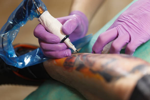istock Tattooist makes new drawing on client leg with modern electric tattoo machine in the studio 1475491549