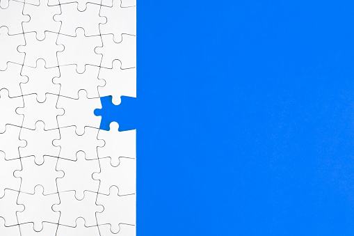 High angle view of jigsaw piece and puzzle on blue background with copy space