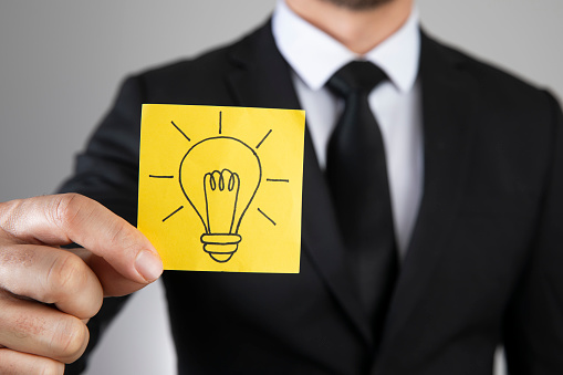 Businessman is holding adhesive note with idea bulb drawing