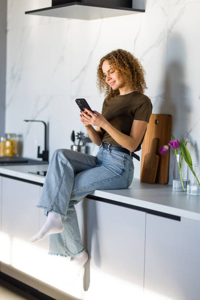 istock Young beautiful woman using cell phone and having a coffee in the kitchen 1475492398