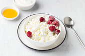 Fresh homemade cottage cheese with frozen raspberries, honey and sour cream on a light gray background