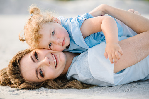 Mother and daughter lying on the sand together outdoors. Mom hugging a little kid girl in nature. Girls on the sandy beach. Mother's day. Family and childhood concept. Close up.