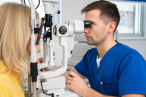 Caucasian male ophthalmologist examining with slit lamp structures of the eye, such as the cornea, iris, and lens, on a senior female patient at the ophthalmology clinic
