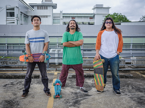 Small Group of young Asian skateboarder man holding skateboard standing at rooftop parking outdoors, Active Lifestyle, Looking at camera