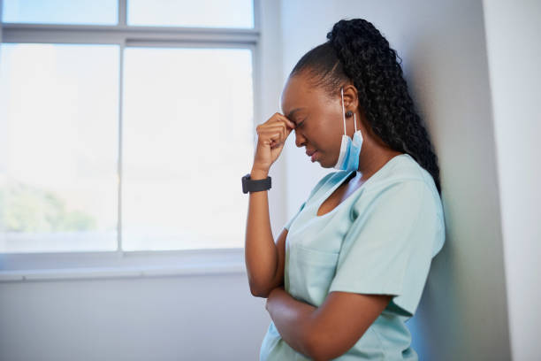Young nurse or doctor in scrubs leans against wall, overworked stressed stock photo