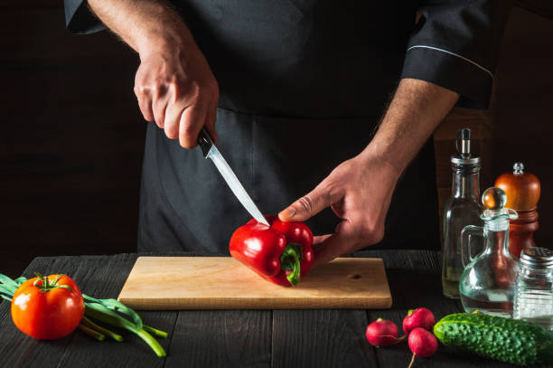 istock Professional chef or cook is cutting red peppers for salad on a restaurant kitchen table. Vegetable diet or snack idea 1475512426