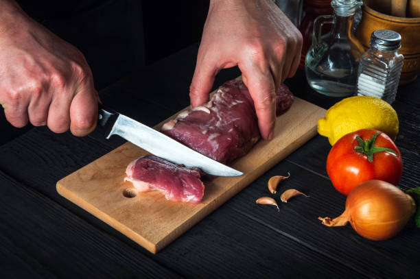 istock Chef cutting beef meat with knife on kitchen, cooking food. Vegetables and spices on kitchen table to prepare delicious lunch 1475512455