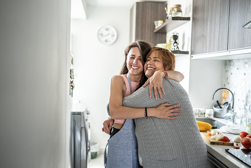 Mother and daughter embracing in the kitchen at home
