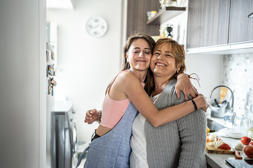 Mother and daughter embracing in the kitchen at home