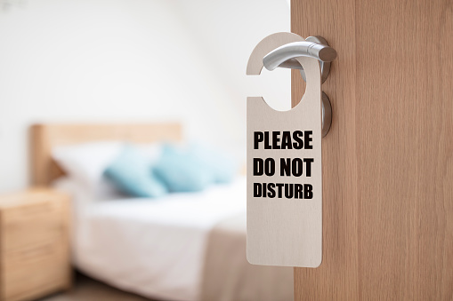 Do not disturb sign on hotel room or apartment door with bedroom and bed in background